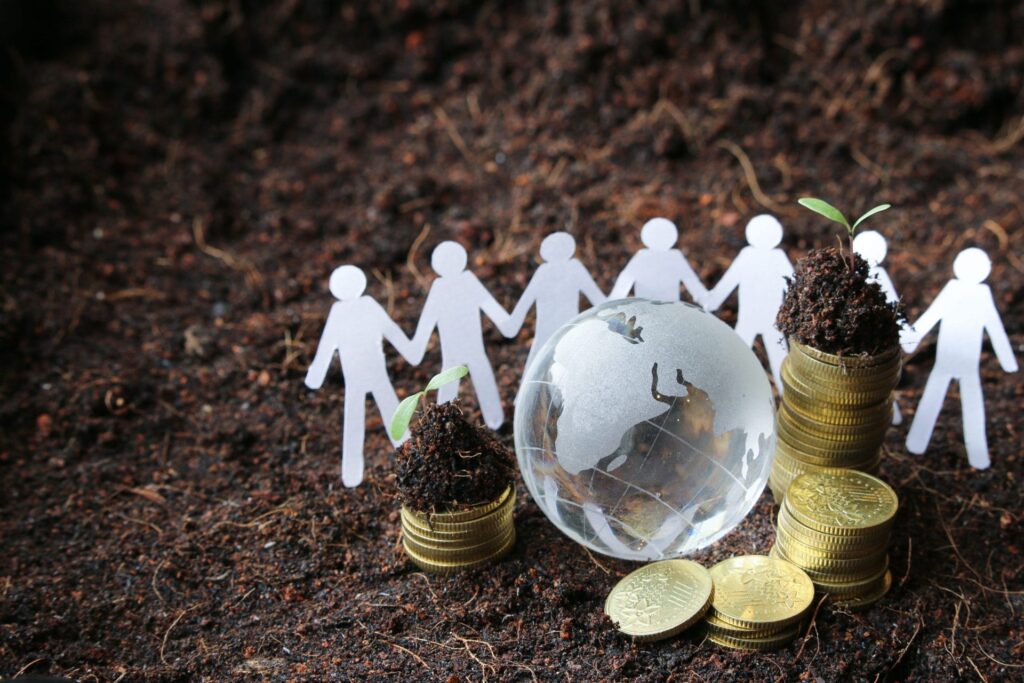 Aufnahme einer Menschenkette aus Papier, die vor einem kleinem Globus stehen und einem Münzhaufen