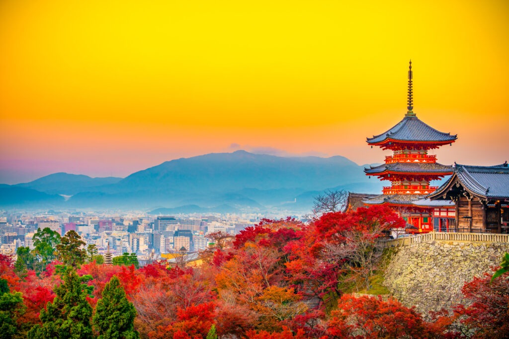 traditionelle japanischer Tempel auf r einem Hügel mit Blick über die Stadt Kyoto, umgeben von roten Herbstbäumen und Bergen im Hintergrund
